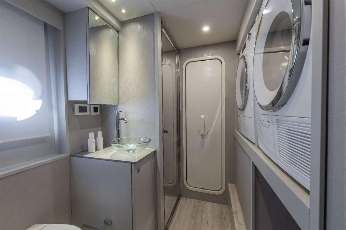 Modern bathroom featuring a glass sink, washing machine, dryer, and shower, with soft lighting and neutral decor.